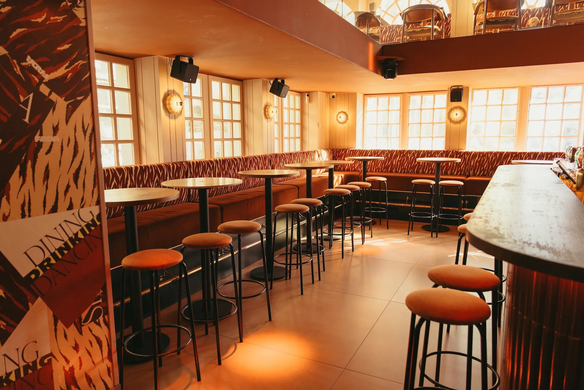 Des tables hautes et tabourets le long d'une banquette sous les fenêtres, le comptoir au premier plan