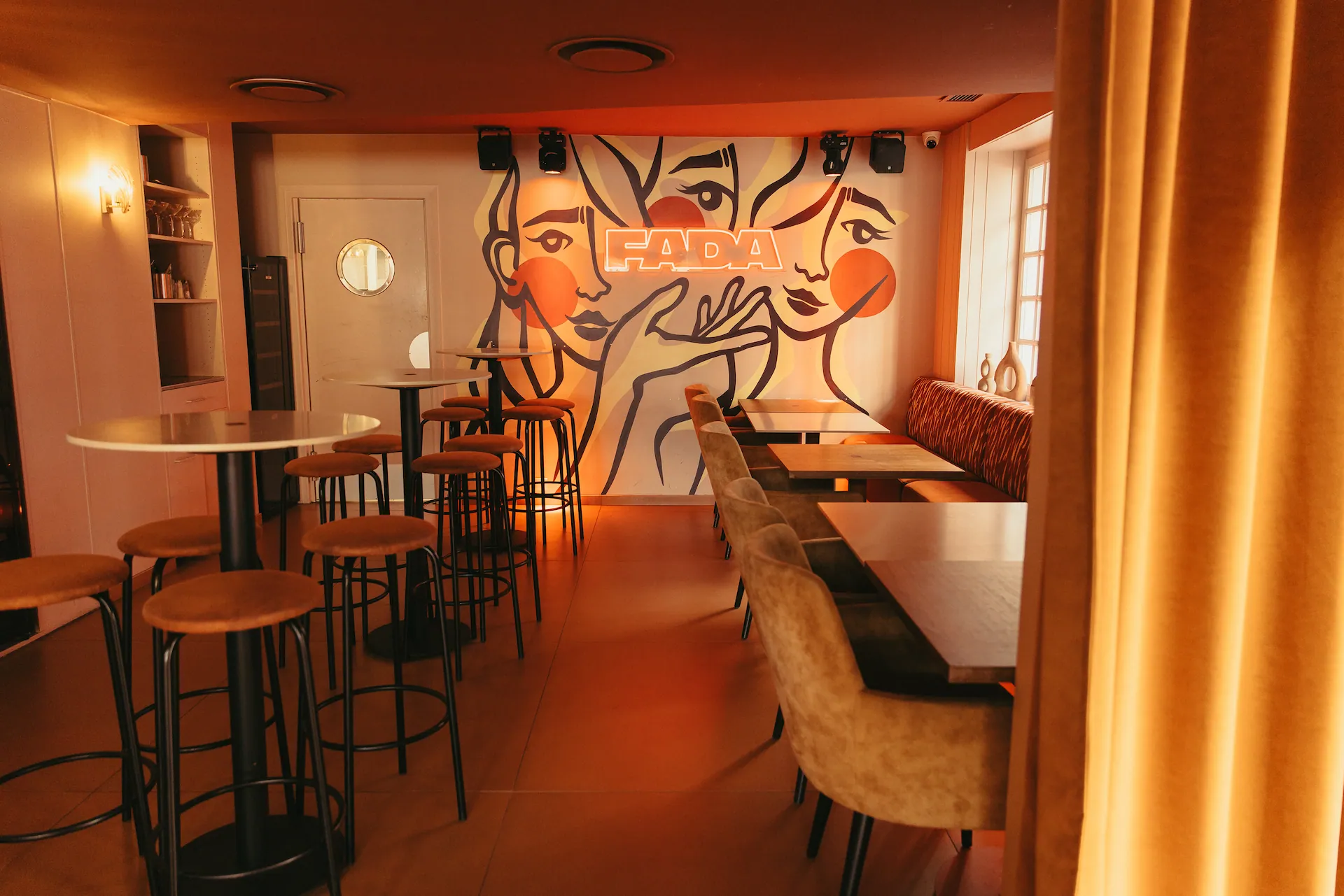 Tables hautes et banquettes devant la fresque FADA, un rideau doré au premier plan
