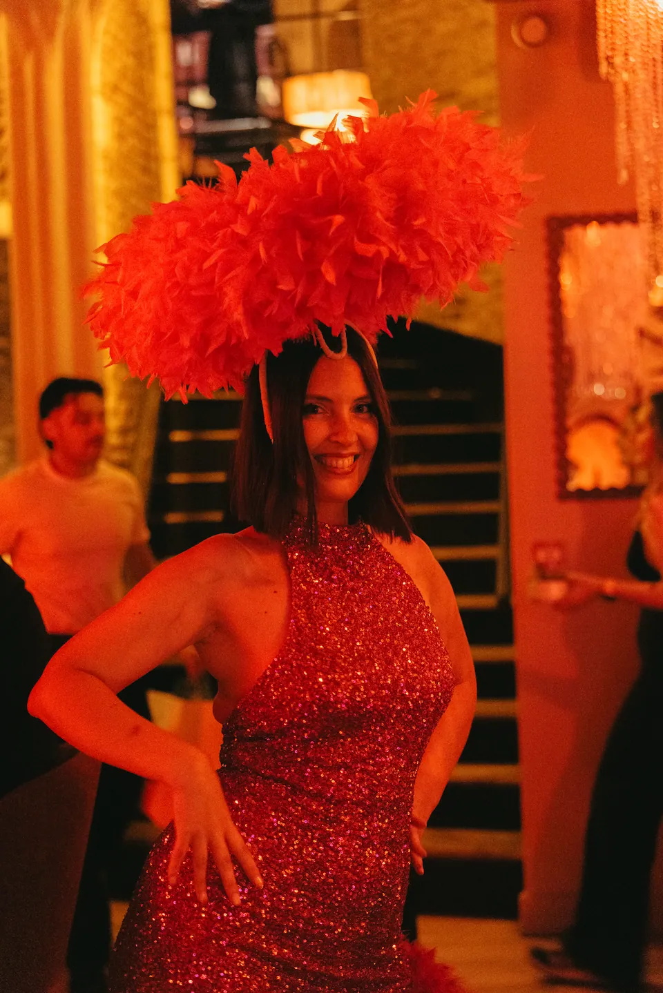 Un numéro de revue au milieu des invités : robe à paillettes et coiffe de plumes rouges