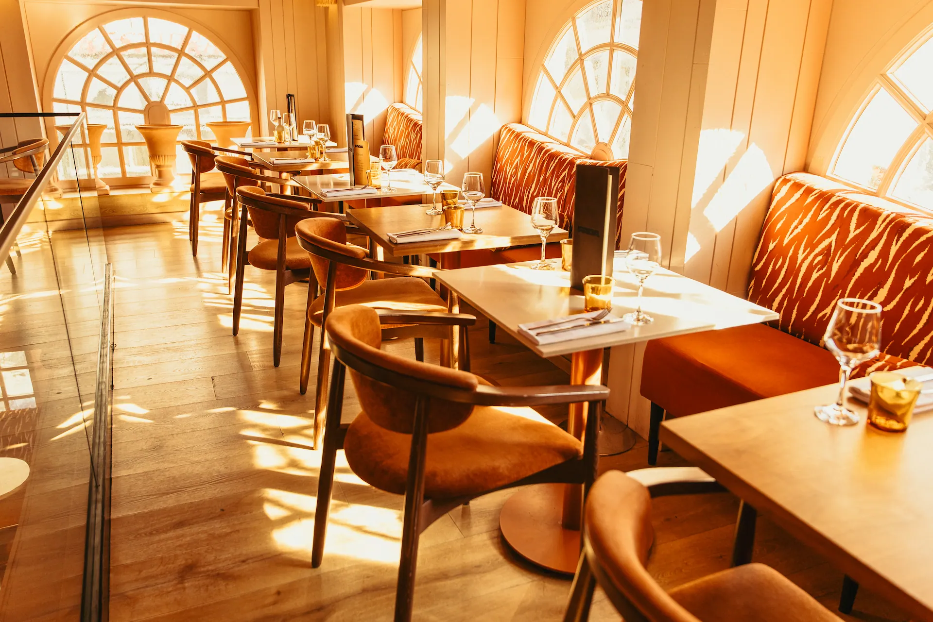 Des tables le long des grandes fenêtres cintrées, le soleil sur les banquettes à motif tigré
